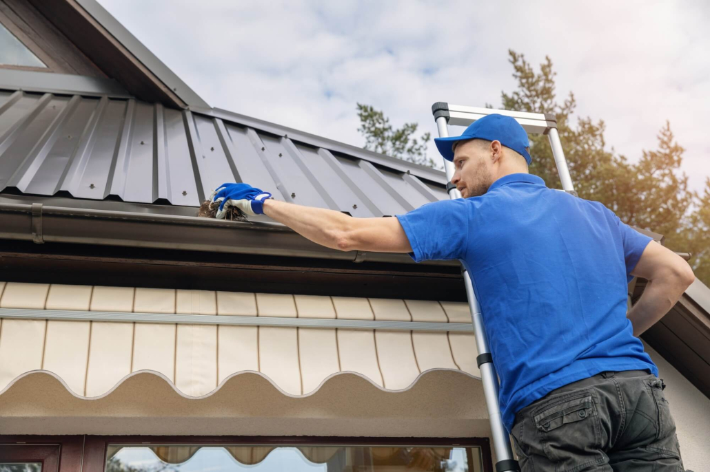 A man standing on ladder and cleaning roof rain gutter from dirt.