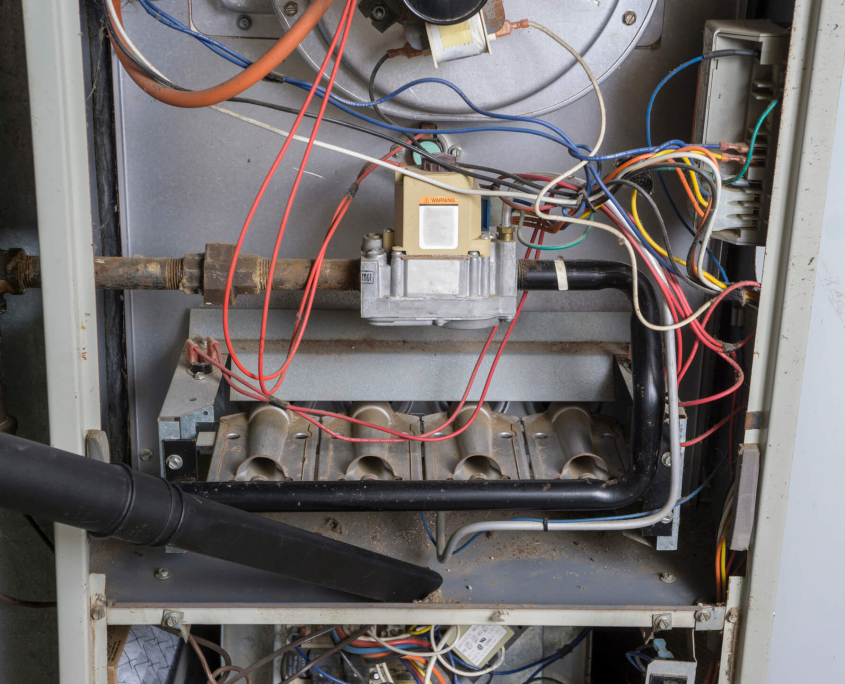Cleaning specialist vacuuming inside of a gas furnace during a cleaning.